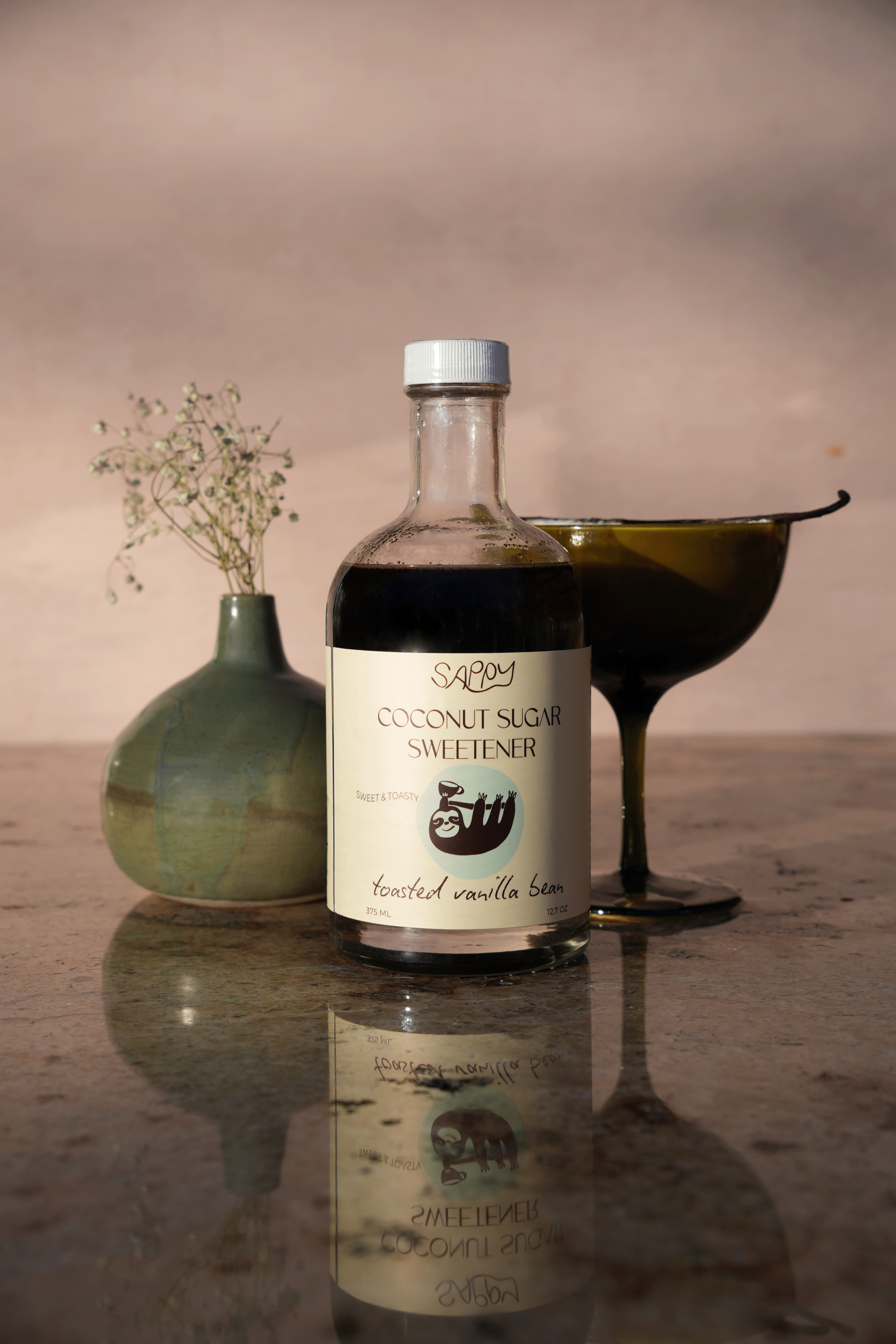 Bottle of coconut sugar sweetener on a reflective surface with a vase and pitcher in the background.